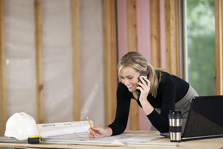 Bauversicherung bei Neubau und Umbau - Frau mit Bauplänen telefoniert