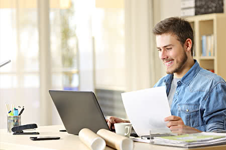 versicherungscheck24.de – Bauleistungsversicherung – Vergleich – Junger Mann sitzt am Laptop und ist fröhlich