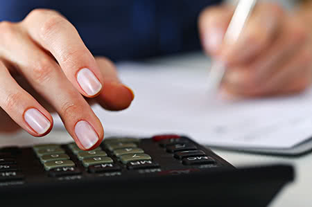 versicherungscheck24.de – Hausratversicherung – Höhe – Frau mit Taschenrechner am Schreibtisch