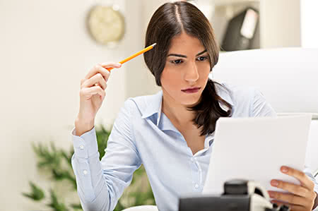 versicherungscheck24.de – Hausratversicherung wechseln – Frau sitzt nachdenklich am Schreibtisch über Dokumenten