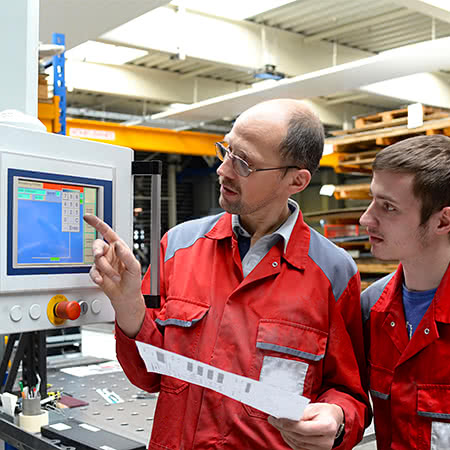 versicherungscheck24.de – Arbeiter schauen sich Bildschirmanzeige an Maschine an