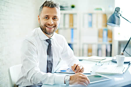 versicherungscheck24.de – Pflegeversicherung – Arbeitgeberanteil – Freundlicher Chef am Schreibtisch