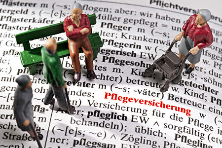 versicherungscheck24.de – Pflegeversicherung – Pflegeversicherungsgesetz – Kleine Seniorenfiguren stehen auf Zeitungsartikel mit dem Thema Pflegeversicherung