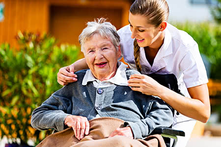 versicherungscheck24.de – Pflegeversicherung – Pflegerin hält Hand von Seniorin im Rollstuhl