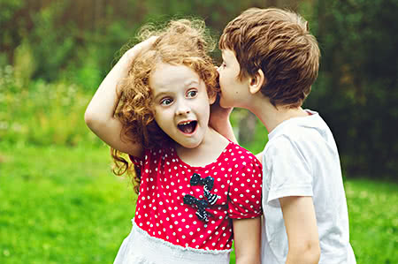 versicherungscheck24.de – Rechtsschutzversicherung – Familie – Zwei Kinder flüstern sich etwas ins Ohr