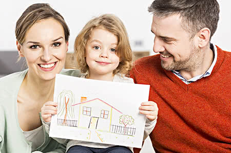 versicherungscheck24.de – Wohngebäudeversicherung – Fertighaus – Familie und Kind hält gemaltes Bild mit Haus hoch