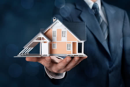 Bauversicherung Schweiz - Versicherer mit einem Haus Modell auf der Hand
