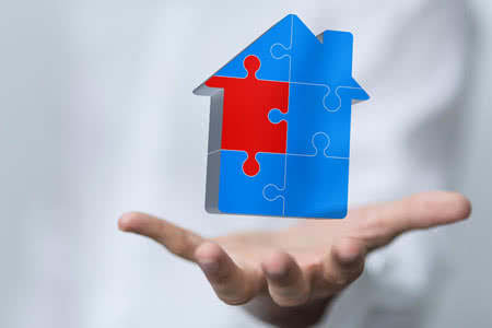 Was sollte eine Wohngebäudeversicherung beinhalten? - Hand mit einem Haus aus Puzzle